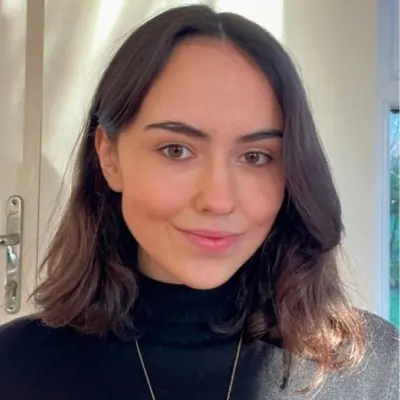 Portrait of a young woman with brown hair and a black turtleneck, smiling softly.