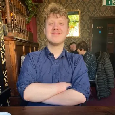 Young man with curly hair smiling in a cozy restaurant setting.